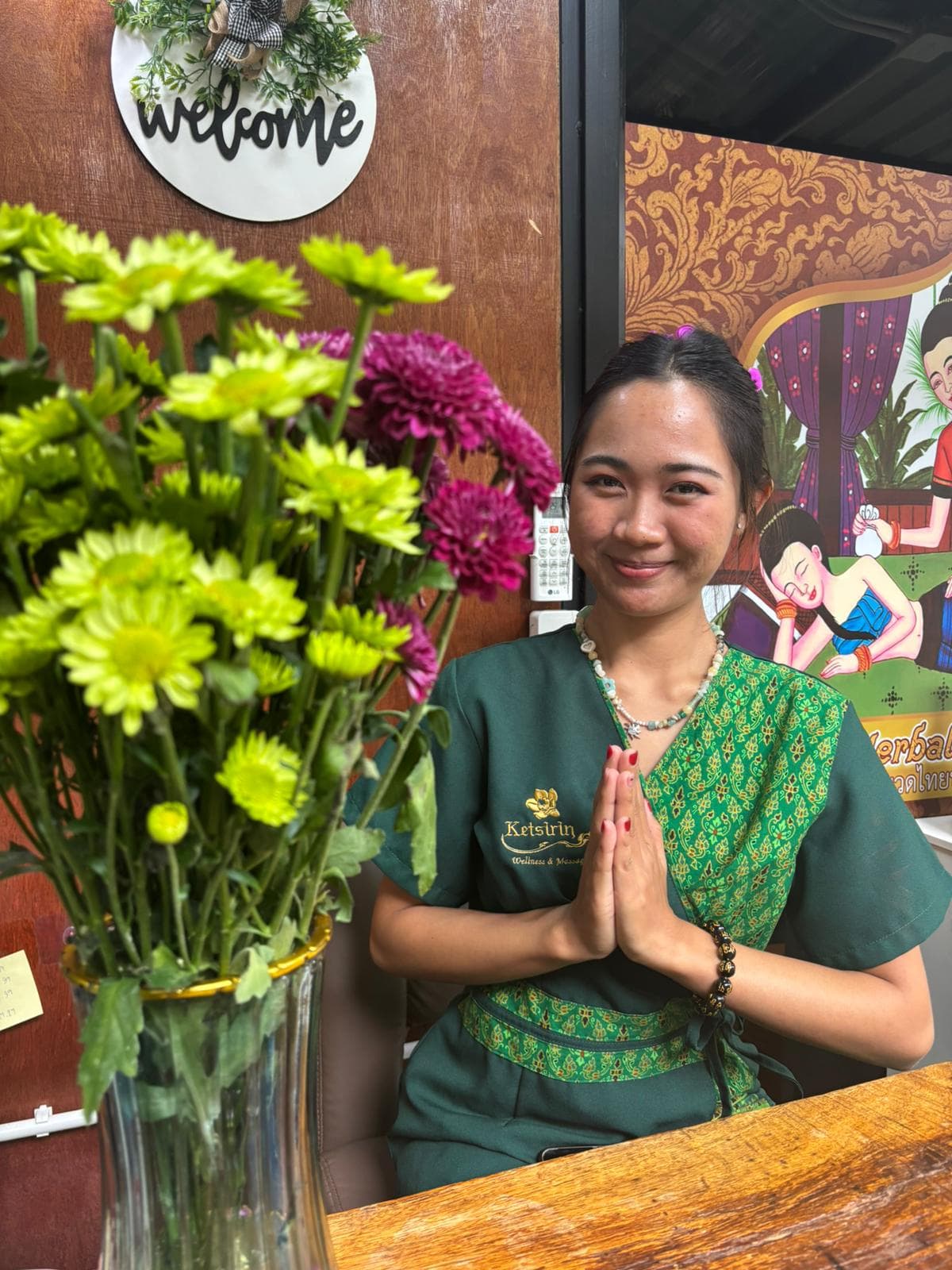 Friendly staff member at reception with traditional Thai greeting and fresh flowers