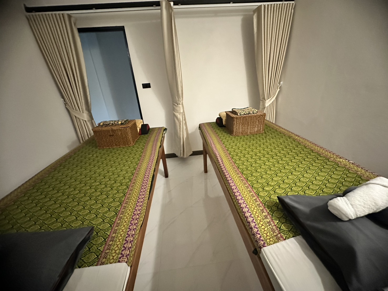 Thai massage treatment room with two beds featuring traditional green patterned fabric and privacy curtains