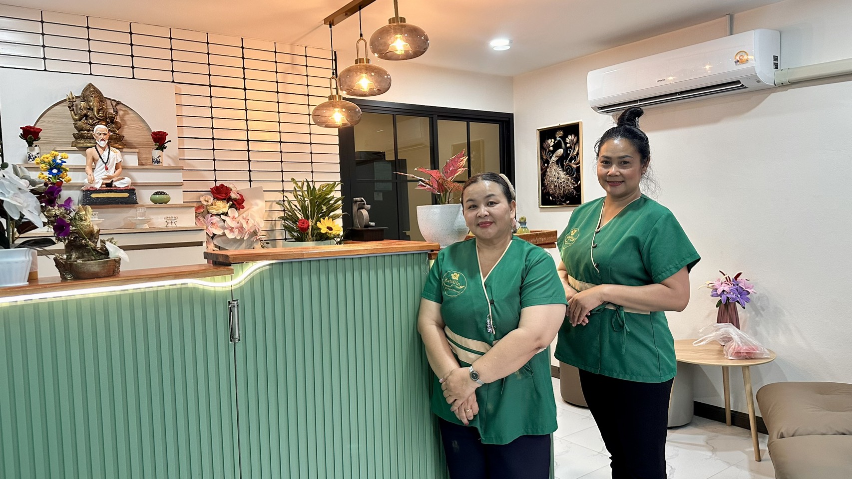 Ketsirin therapists standing by the reception counter with Thai massage shrine and decorative flowers
