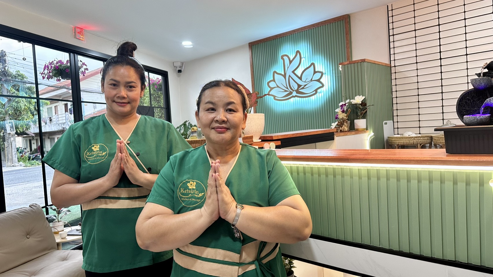 Friendly Ketsirin therapists in green uniforms giving traditional Thai wai greeting at Cherngtalay reception