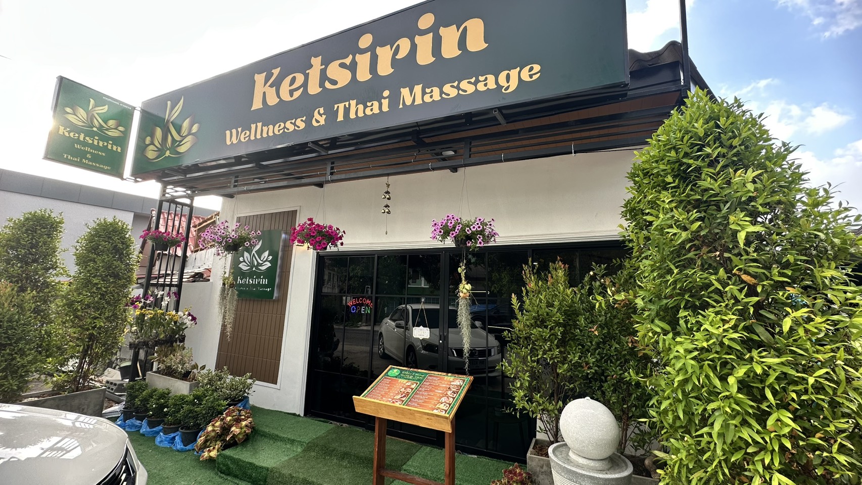 Ketsirin Wellness & Thai Massage Cherngtalay storefront with gold signage, hanging flower baskets and lush greenery